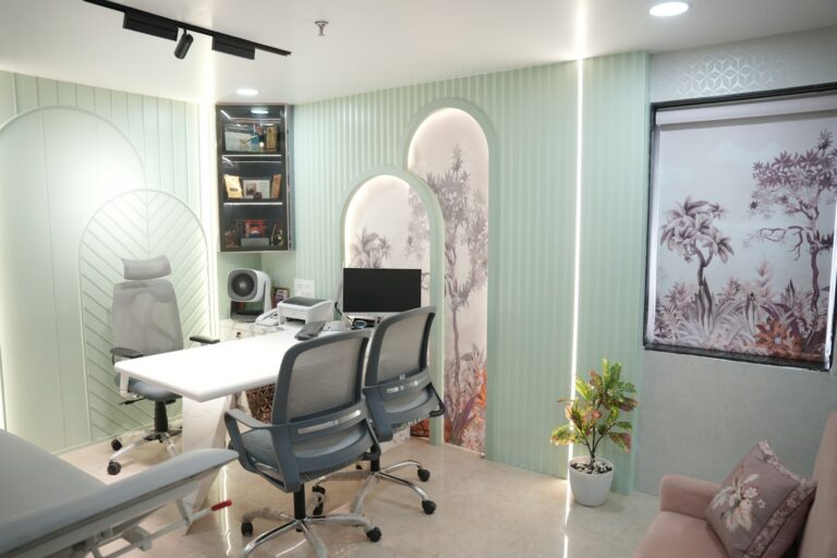 Modern office/consultation room with mint green striped walls, a white desk, and two gray mesh chairs facing a computer.